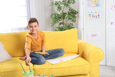 Photo of Little boy painting picture on sofa indoors