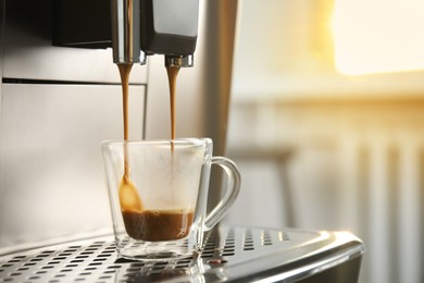 Photo of Espresso machine pouring coffee into glass cup against blurred background, closeup. Space for text