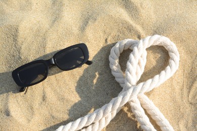 Photo of Stylish sunglasses and rope on sand, flat lay