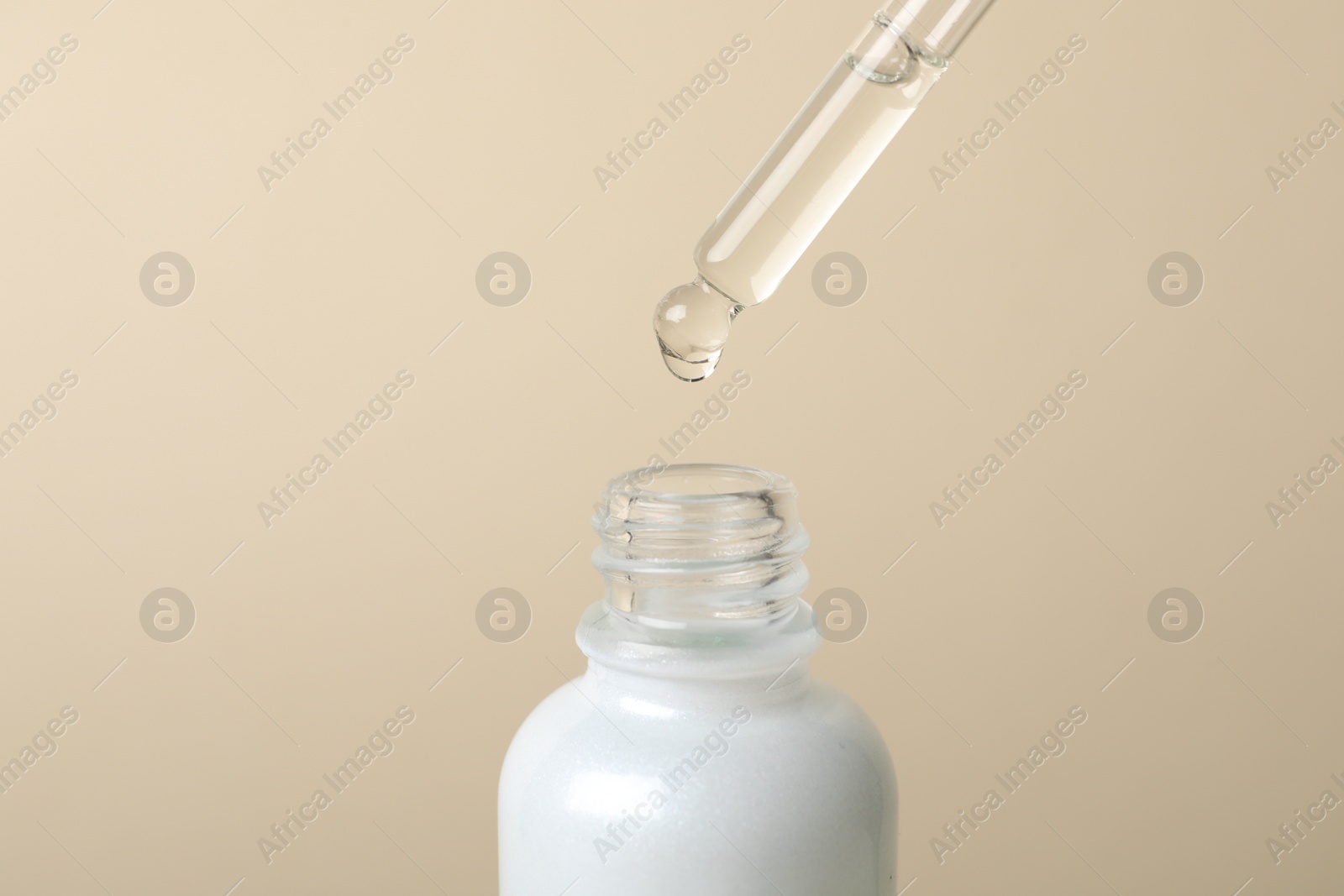 Photo of Dripping cosmetic serum from pipette into bottle on beige background, space for text