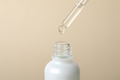 Photo of Dripping cosmetic serum from pipette into bottle on beige background, space for text