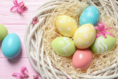 Photo of Flat lay composition of wicker nest with painted Easter eggs on wooden table