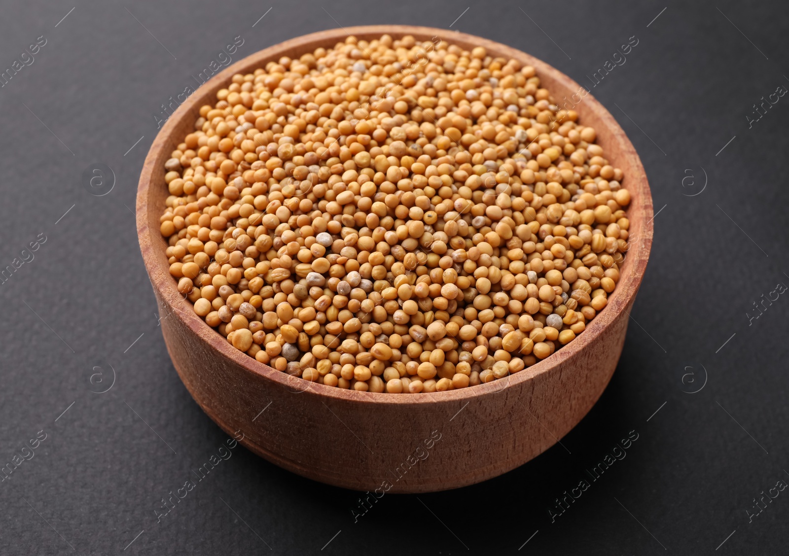 Photo of Wooden bowl with mustard seeds on grey background