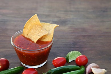 Tasty salsa sauce with tortilla chips and ingredients on wooden table, closeup. Space for text
