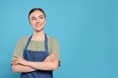 Photo of Beautiful young woman in clean denim apron on light blue background. Space for text