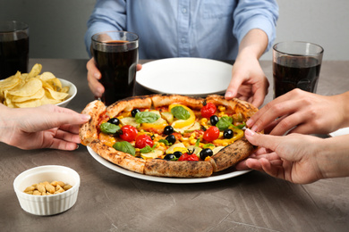 Women taking slices of delicious vegetable pizza at grey table, closeup