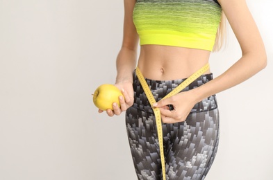 Photo of Woman with fresh apple and measuring tape on light background. Healthy diet