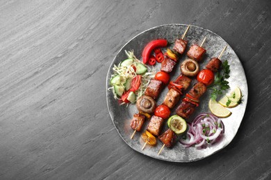 Photo of Delicious shish kebabs with vegetables on grey textured table, top view. Space for text