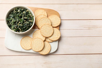 Photo of Tasty spinach dip with eggs in bowl and crackers on light wooden table, top view. Space for text