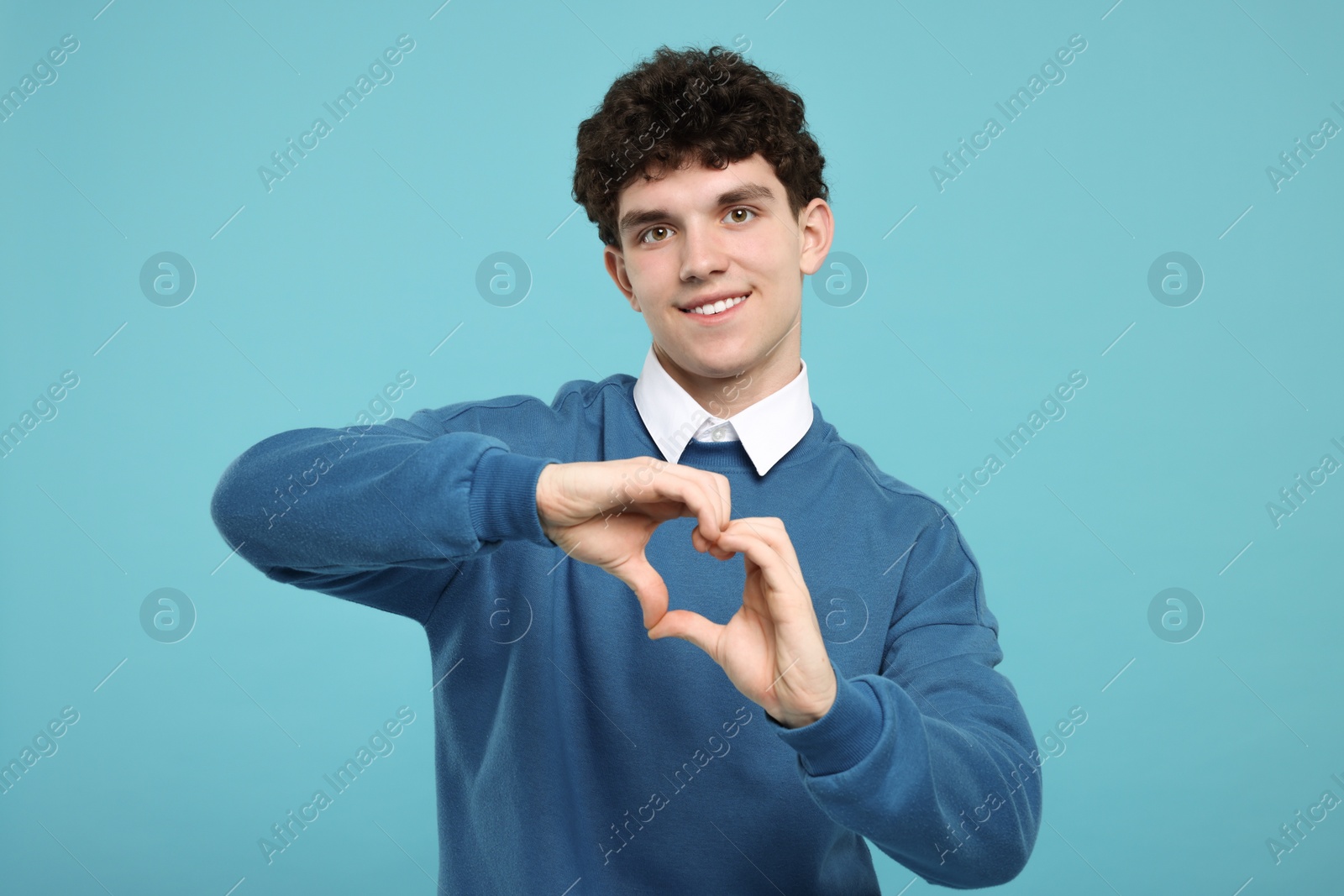 Photo of Happy young man showing heart gesture with hands on light blue background