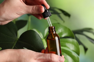 Woman with bottle of cosmetic serum and dropper on green background, closeup