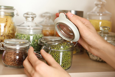 Photo of Woman taking jar of mung beans from wooden shelf, closeup