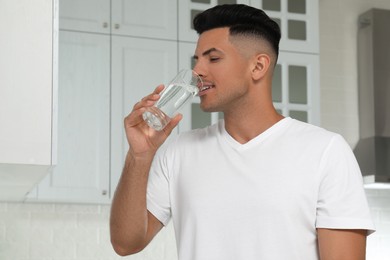 Man drinking tap water from glass in kitchen