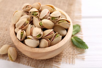 Photo of Tasty pistachios in bowl on white wooden table, closeup