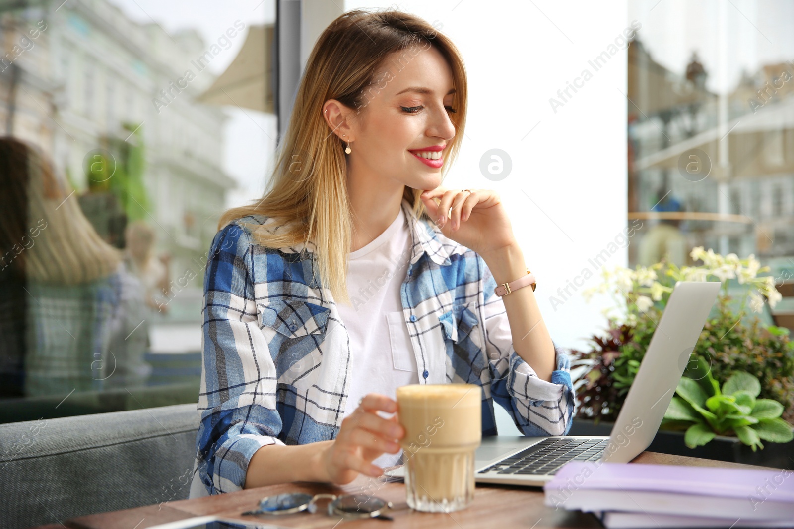 Photo of Young woman working with laptop at desk in cafe