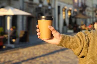 Photo of Woman holding paper takeaway cup on city street, closeup. Coffee to go