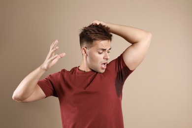 Photo of Young man with sweat stain on his clothes against beige background. Using deodorant