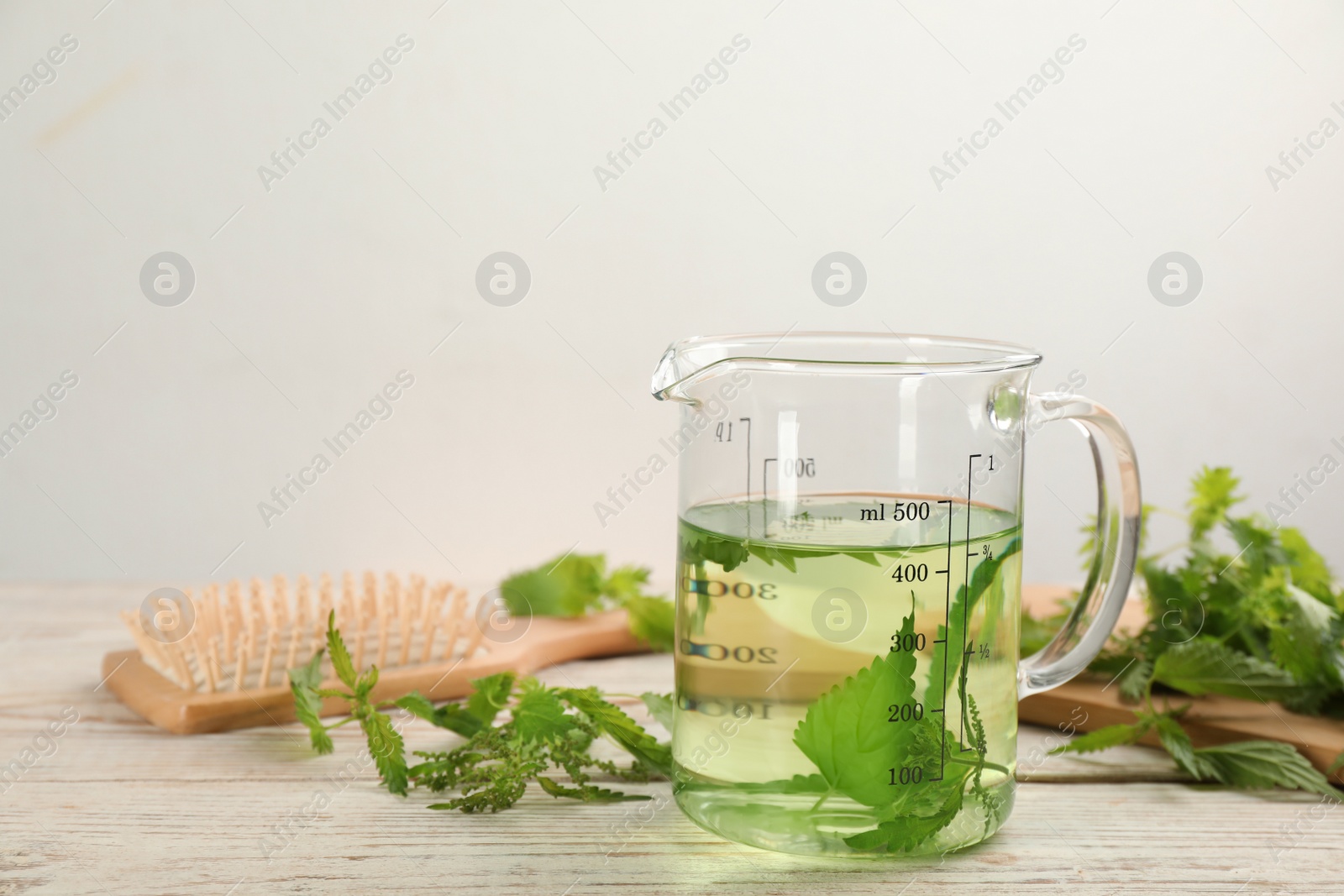 Photo of Stinging nettle, extract and brush on white wooden background. Natural hair care