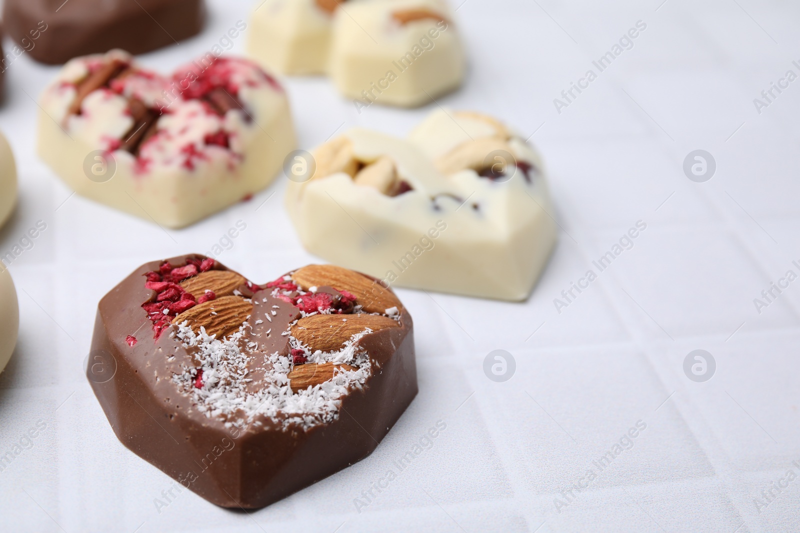 Photo of Tasty chocolate heart shaped candies with nuts on white tiled table, closeup