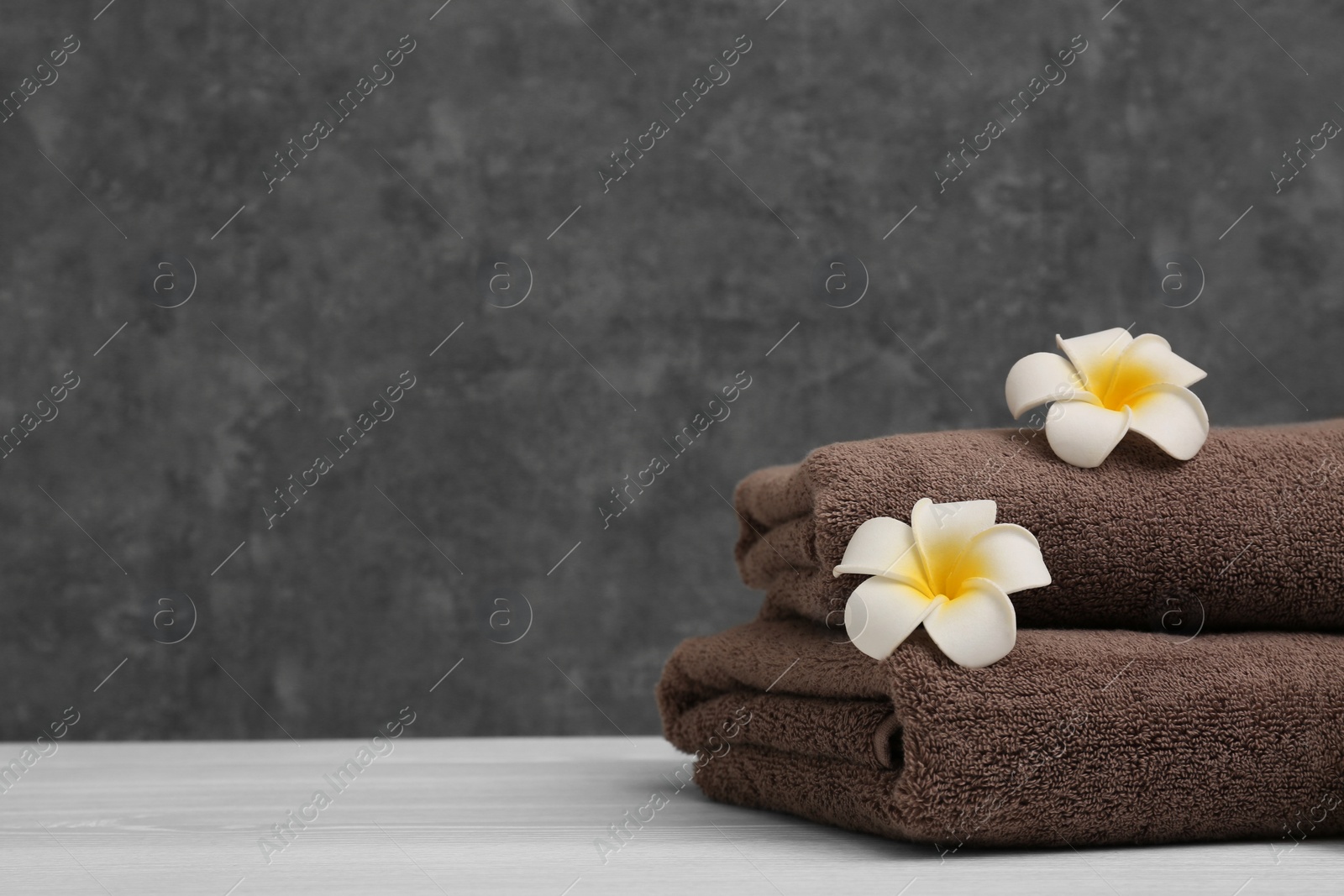 Photo of Stack of soft clean towels with beautiful flowers on table against color background. Space for text