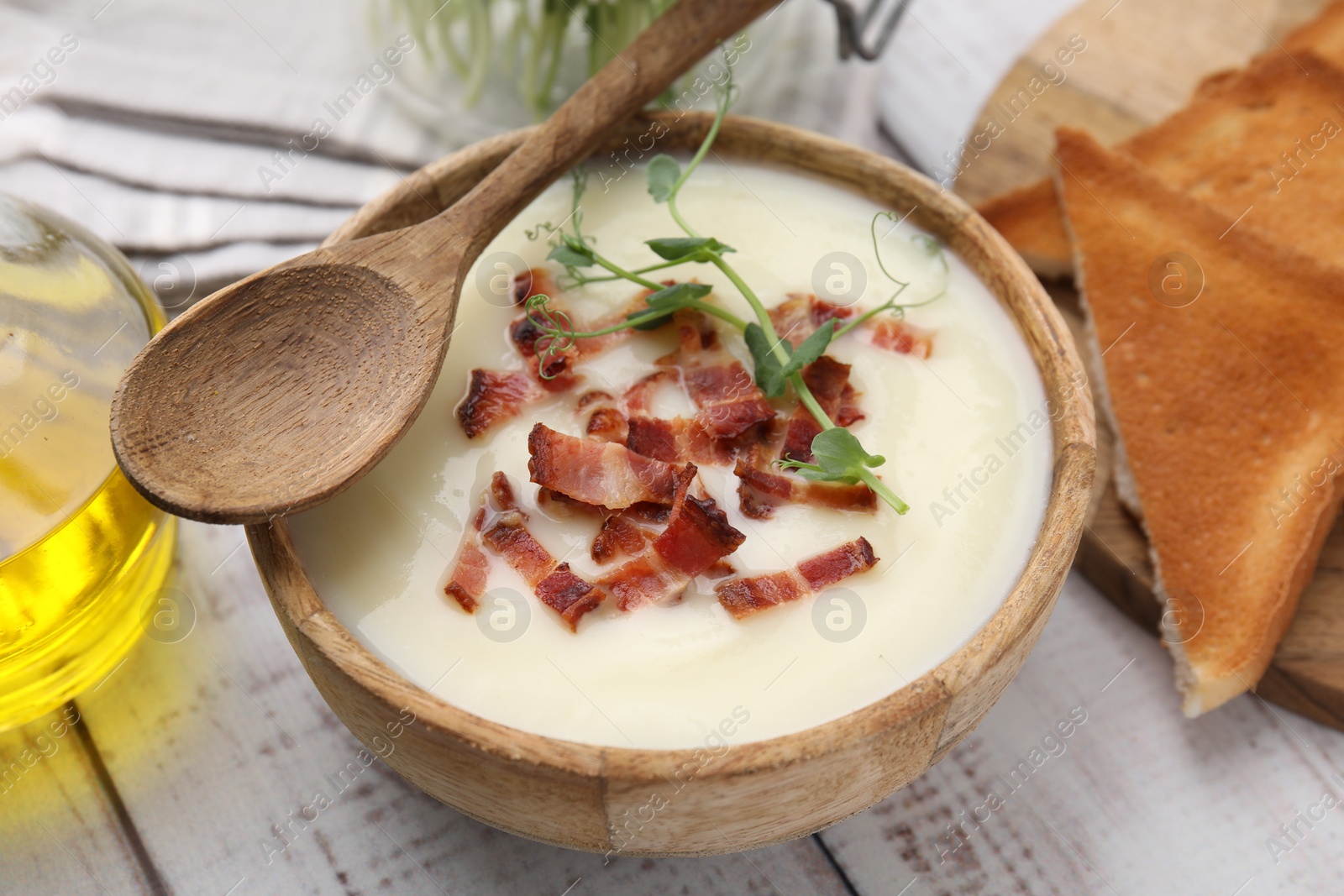 Photo of Delicious potato soup with bacon and microgreens in bowl served on wooden table, closeup