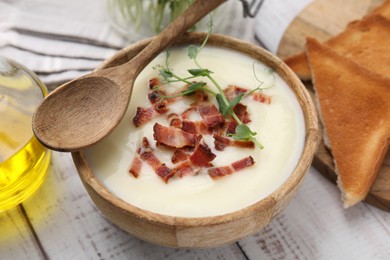 Delicious potato soup with bacon and microgreens in bowl served on wooden table, closeup