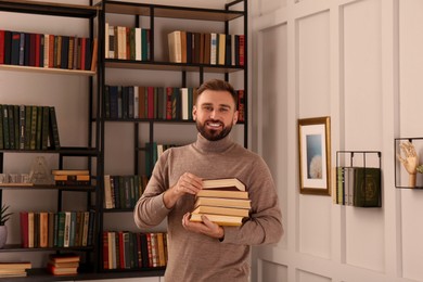 Young man with stack of different books in home library