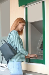 Beautiful woman using cash machine for money withdrawal outdoors