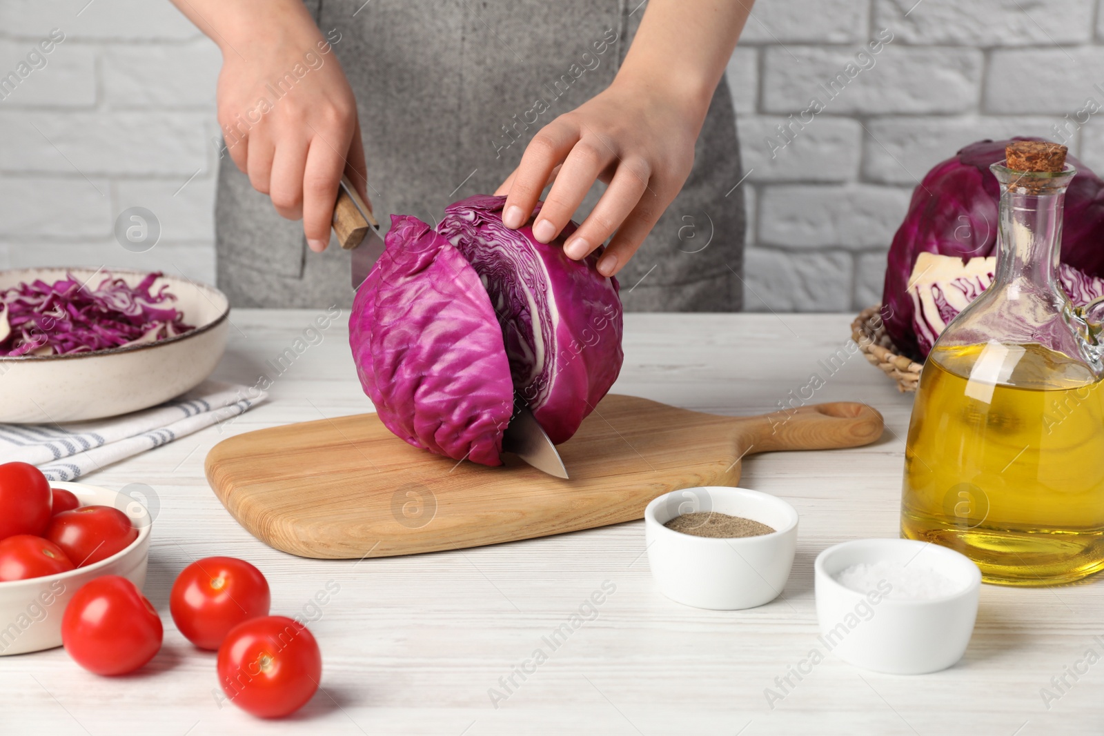 Photo of Woman cutting fresh red cabbage at white wooden table, closeup