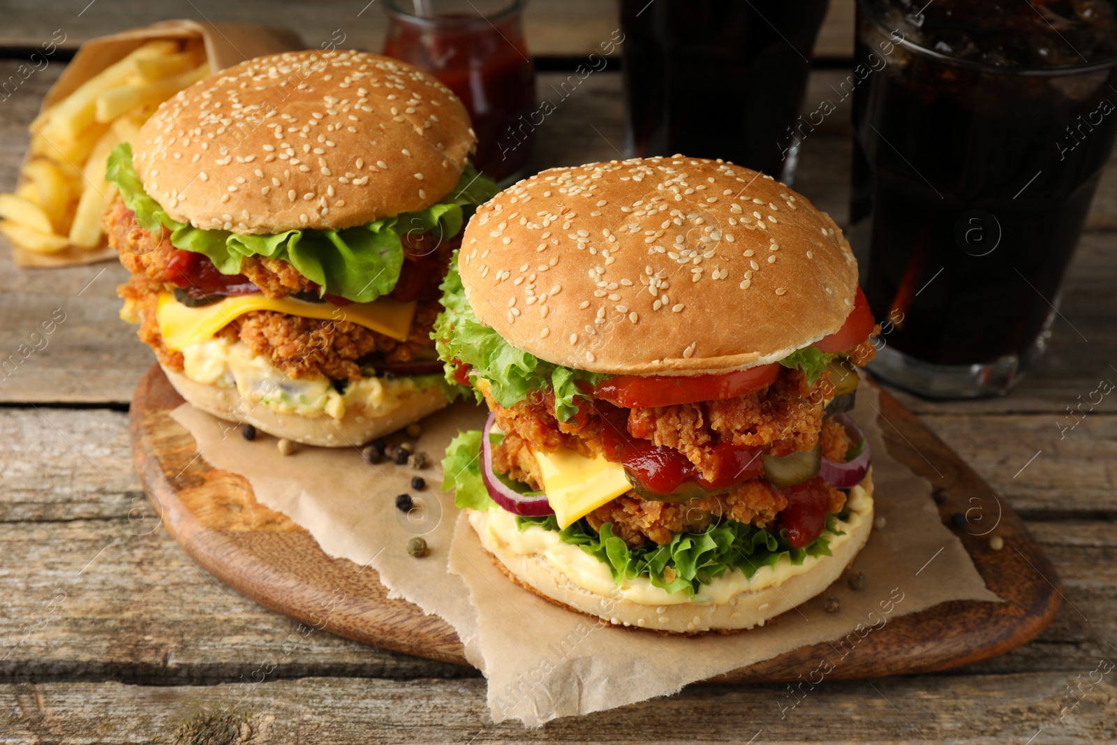 Photo of Delicious burgers with crispy chicken patty, french fries and soda drinks on wooden table