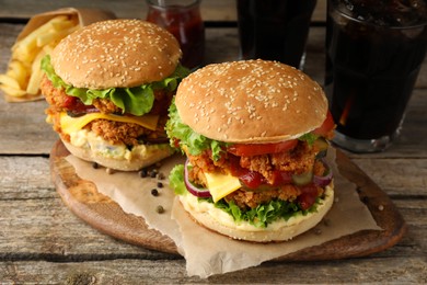 Photo of Delicious burgers with crispy chicken patty, french fries and soda drinks on wooden table
