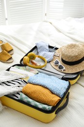 Photo of Open suitcase fullclothes, shoes and summer accessories on bed