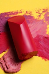 Bright lipstick and different smears on yellow background, top view