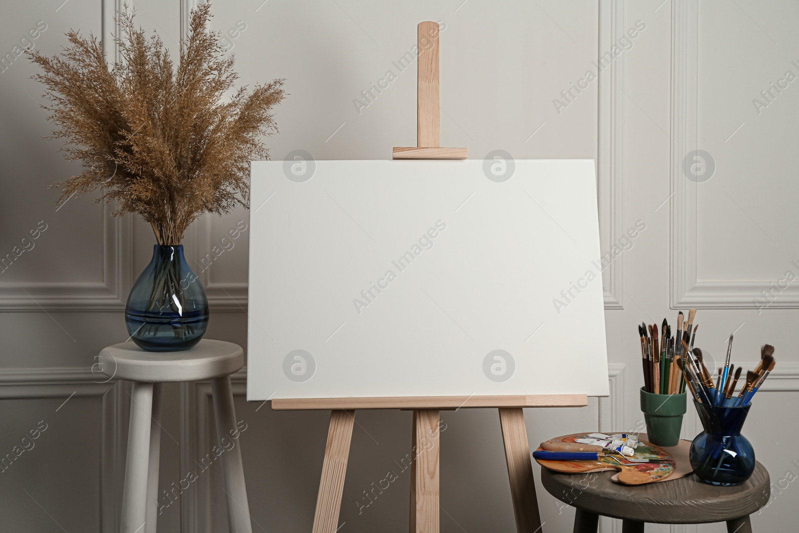 Photo of Easel with blank canvas, brushes, paints and palette in studio