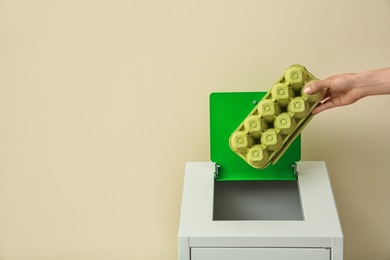 Photo of Woman throwing egg carton into trash bin on color background, closeup with space for text. Recycling concept