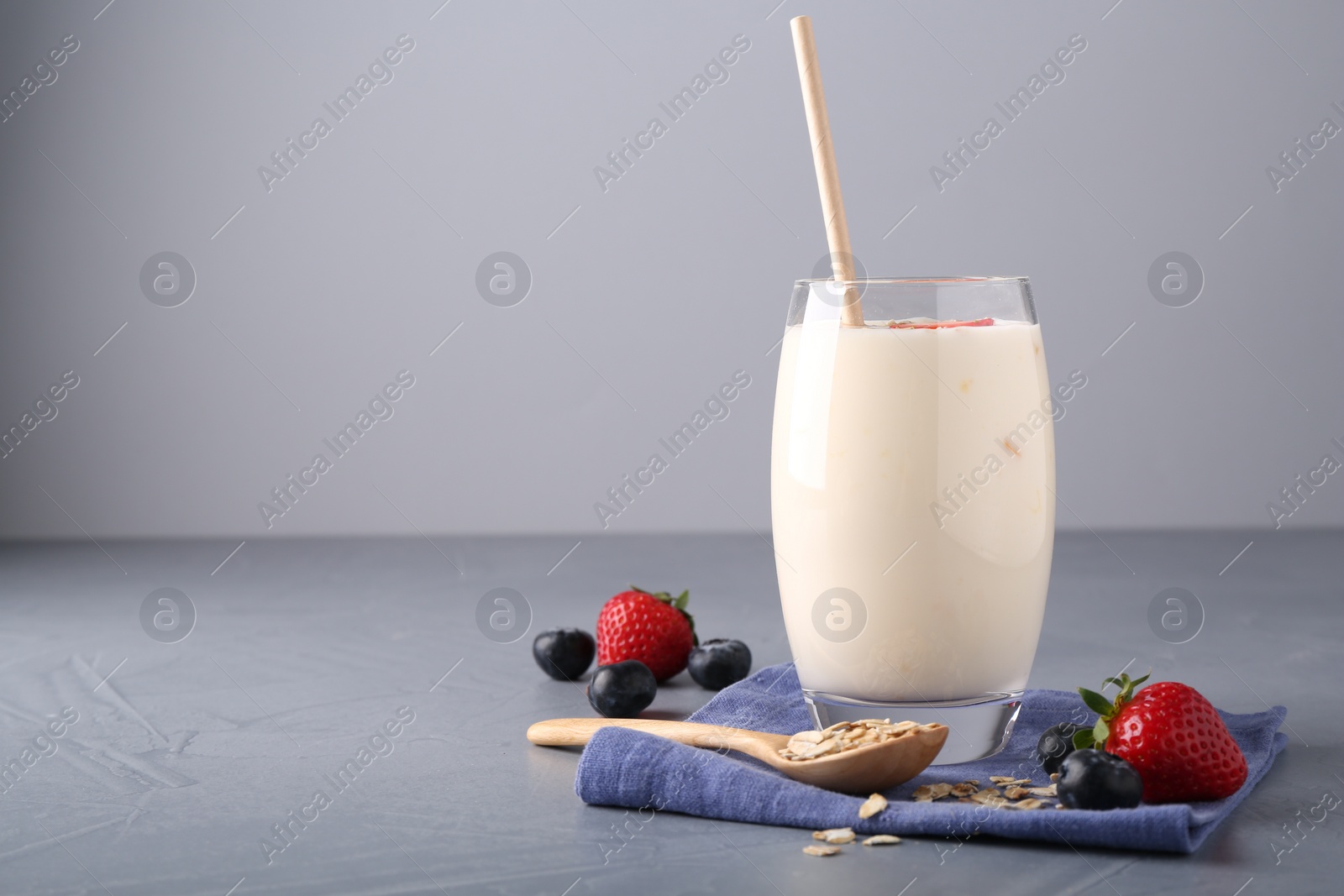 Photo of Tasty yogurt in glass, oats and berries on grey table, space for text