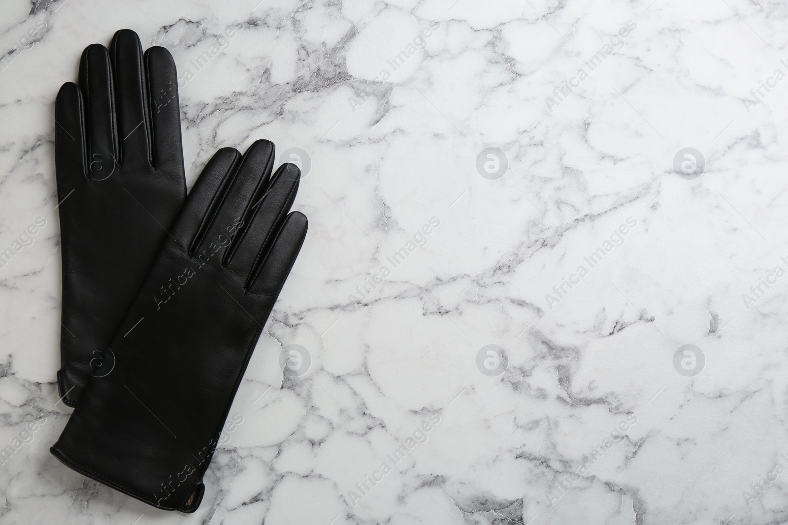 Photo of Stylish black leather gloves on white marble table, flat lay. Space for text
