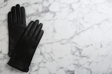 Stylish black leather gloves on white marble table, flat lay. Space for text