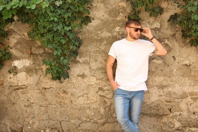 Photo of Young man wearing white t-shirt near stone wall on street