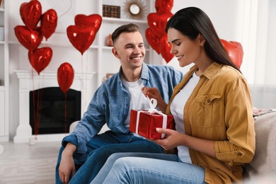 Photo of Woman opening gift from her boyfriend indoors. Valentine's day celebration