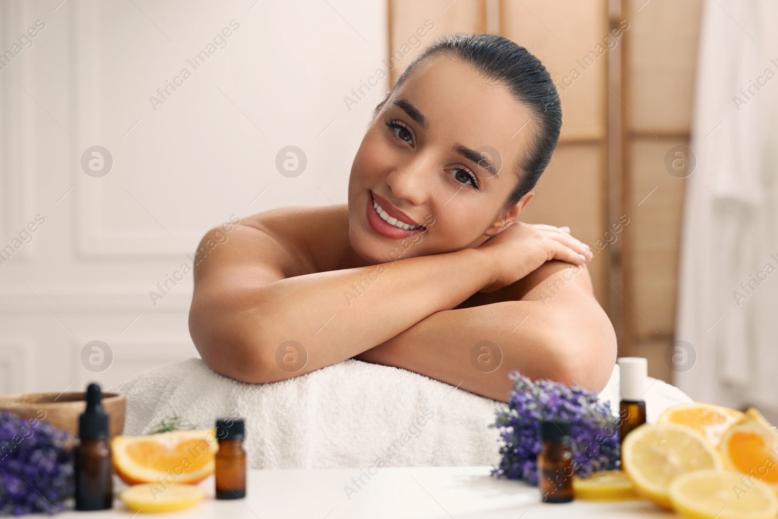 Photo of Beautiful young woman relaxing on massage couch and bottles of essential oil with ingredients on table in spa salon