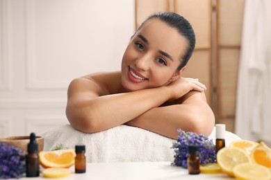 Photo of Beautiful young woman relaxing on massage couch and bottles of essential oil with ingredients on table in spa salon