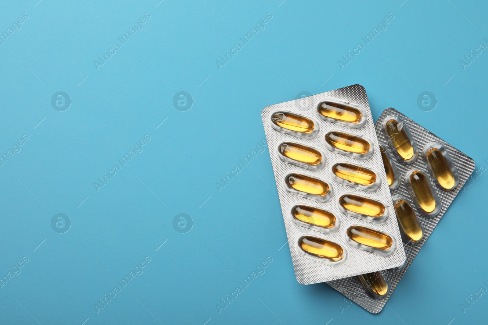 Photo of Dietary supplement capsules in blister packs on light blue background, flat lay. Space for text