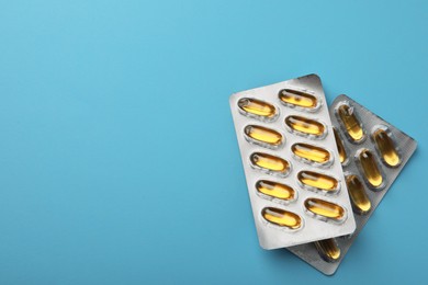 Photo of Dietary supplement capsules in blister packs on light blue background, flat lay. Space for text