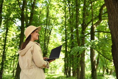 Forester with laptop examining plants in forest, space for text