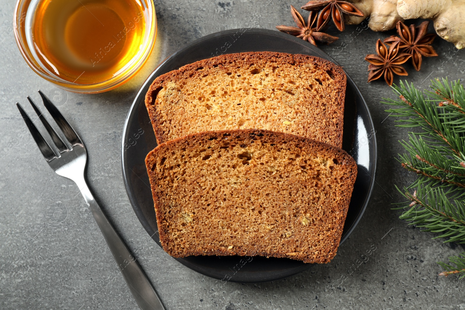 Photo of Fresh gingerbread cake slices served with honey on grey table, flat lay