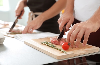 Photo of Male chef cutting meat on wooden board at table, closeup