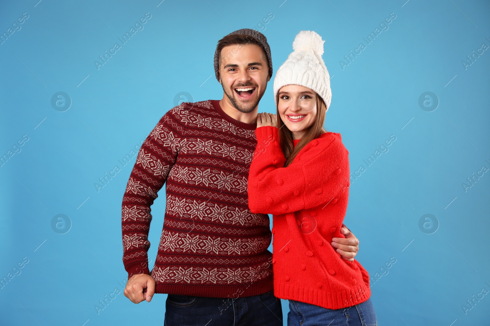 Photo of Couple wearing Christmas sweaters and hats on blue background