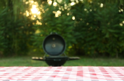 Photo of Picnic table with cloth against blurred barbecue grill outdoors