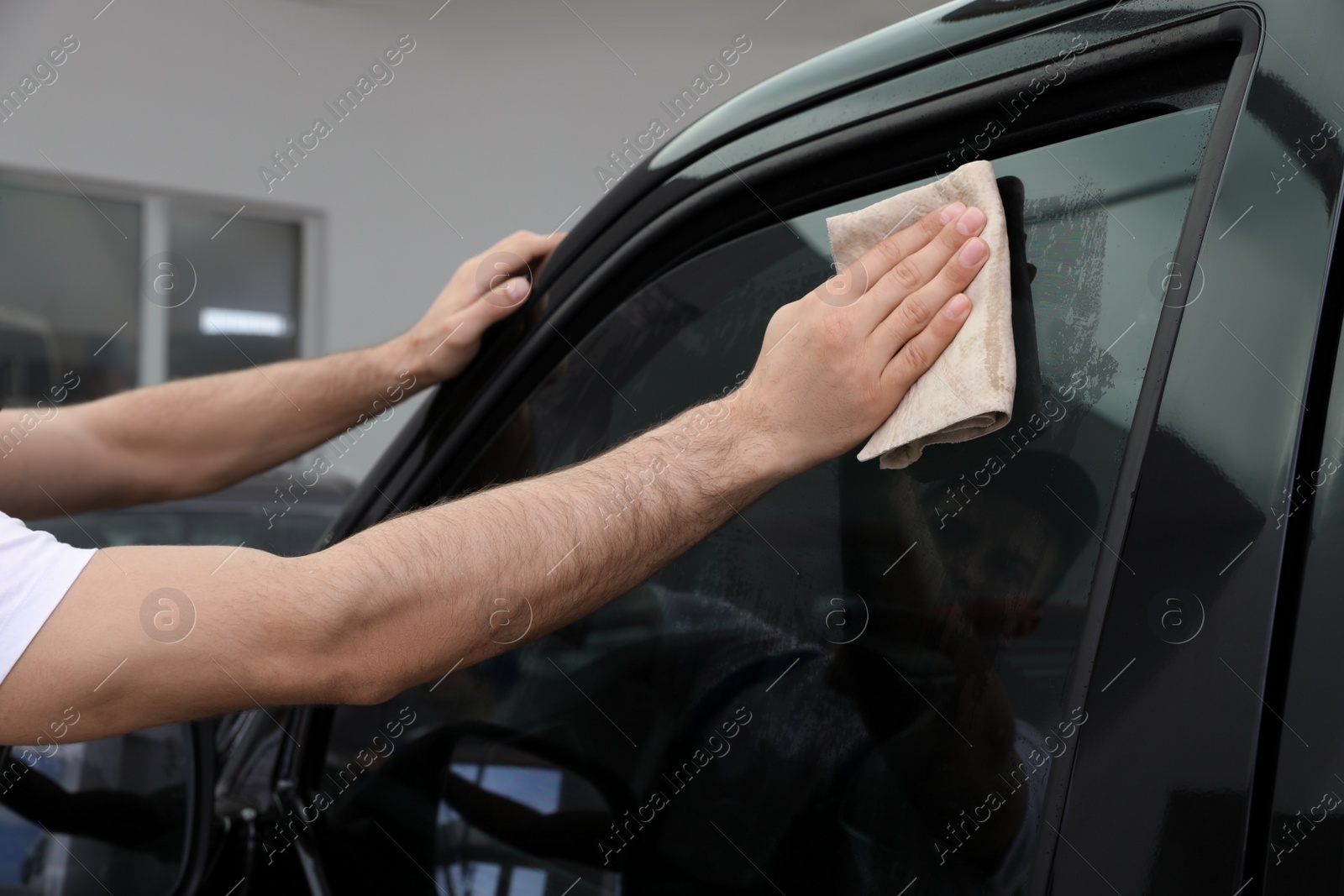 Photo of Worker washing tinted car window in workshop, closeup